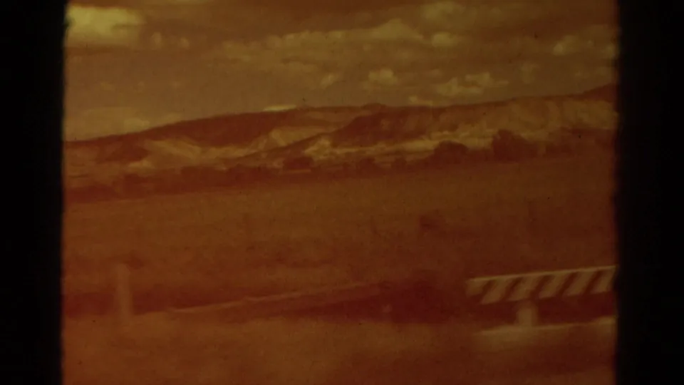 Faded 8mm frame from rural Colorado showing open ground, distant low hills, cloudy sky, and a striped object near the right edge.