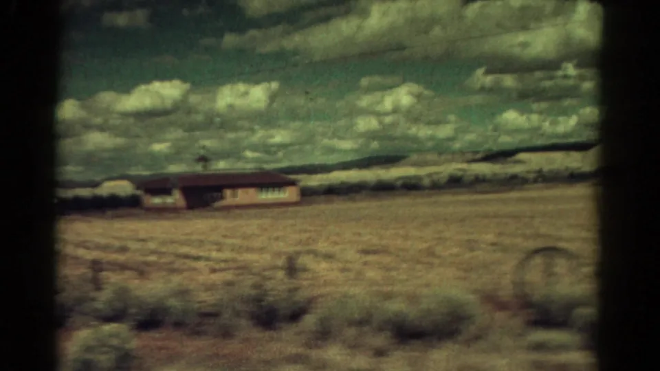 Moving 8mm view in Colorado, 1967, with a low rural building beyond scrubby dry ground and a clouded sky.