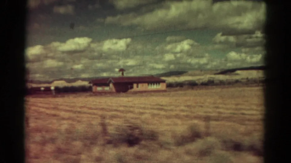 1967 Colorado home-movie frame of a low building across open dry grassland, softened by vehicle motion and film grain.
