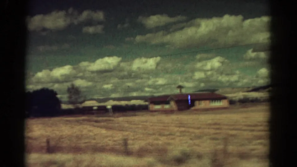 Faded 8mm Colorado frame from 1967 showing a lone low building beside a dry open field and distant hills.