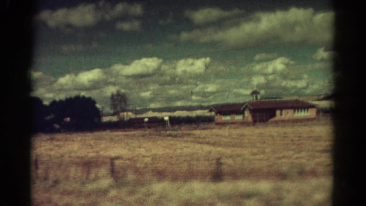 1967 Colorado 8mm frame showing a dry rural field, low house, dark trees, distant hills, and a clouded teal sky.