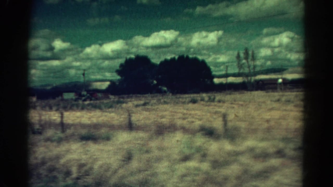 1967 Colorado home-movie view of dry grass, fence posts, trees, and distant hills from a moving vehicle.