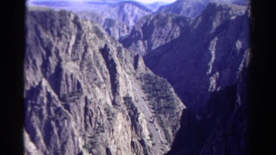 1967 Colorado 8mm frame showing rugged cliffs, a deep shadowed valley, and distant mountain slopes.