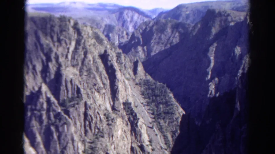1967 Colorado 8mm frame of rocky canyon terrain, tree-dotted slopes, and strong shadow across the valley.