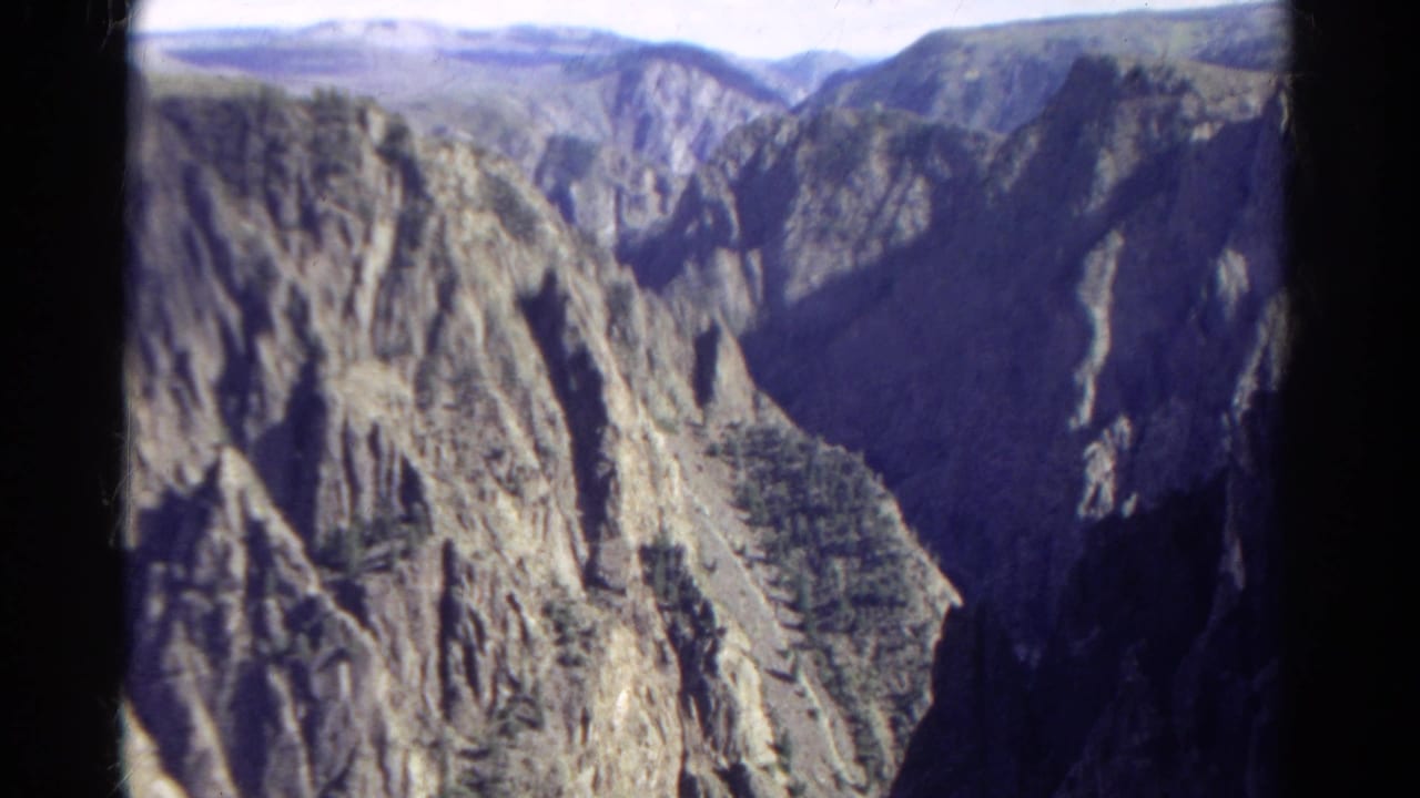 1967 Colorado 8mm frame showing steep canyon walls, jagged rock faces, and a dark valley between sunlit slopes.