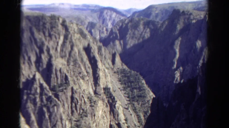 1967 Colorado 8mm frame showing steep canyon walls, jagged rock faces, and a dark valley between sunlit slopes.