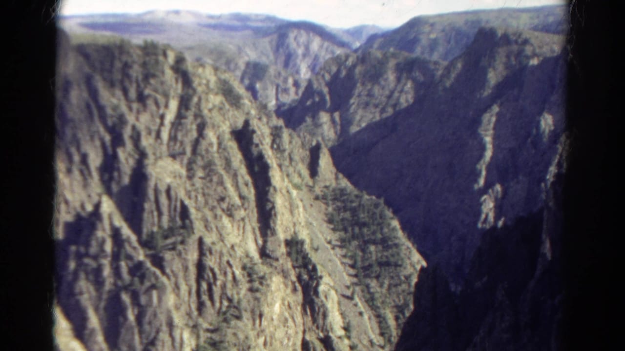 1967 Colorado 8mm view of a deep canyon with rugged ridges, dark shadowed walls, and pale distant uplands.