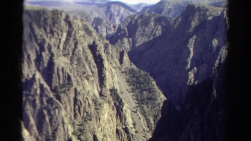 1967 Colorado 8mm frame with steep cliff faces, a narrow shadowed valley, and small patches of green vegetation.