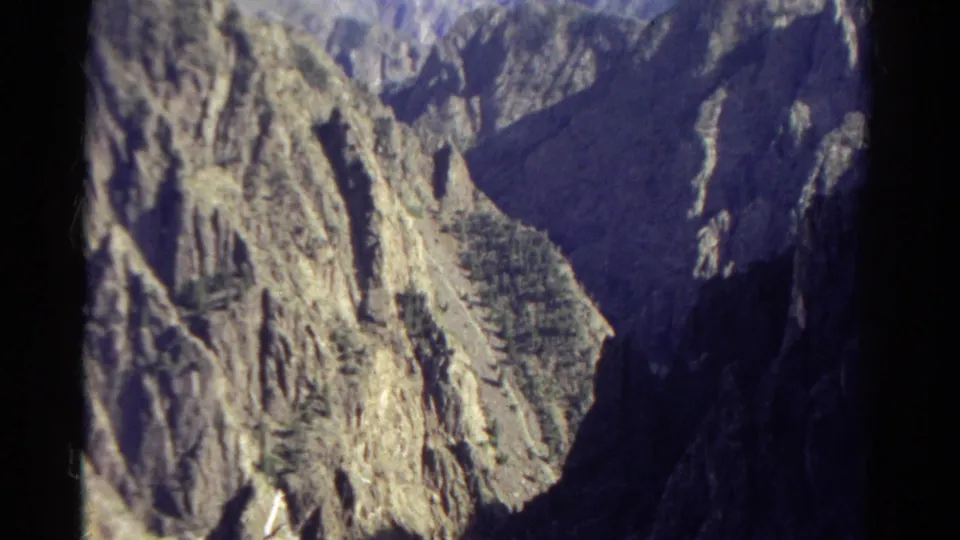 1967 Colorado 8mm frame showing rough canyon rock, a broad dark slope, and sunlit cliff detail near the valley edge.