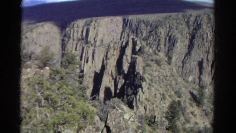1967 Colorado 8mm frame looking across a rugged canyon wall, with jagged rock formations, scrub vegetation, and soft handheld focus.