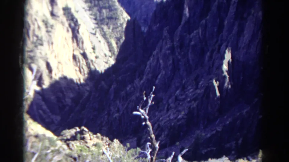 1967 Colorado home-movie frame showing dead branches and scrub before a high-contrast mountain canyon wall.
