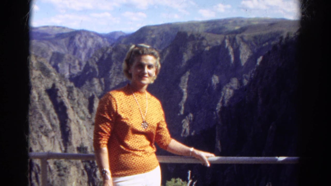 A woman poses at a Colorado canyon overlook in 1967, framed by a metal rail and broad rocky cliffs.