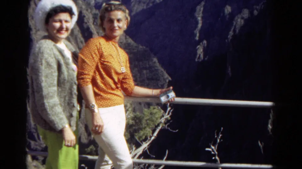 Two women in bright late-1960s clothing stand close together at a Colorado overlook, framed by a railing and shadowed canyon rock.