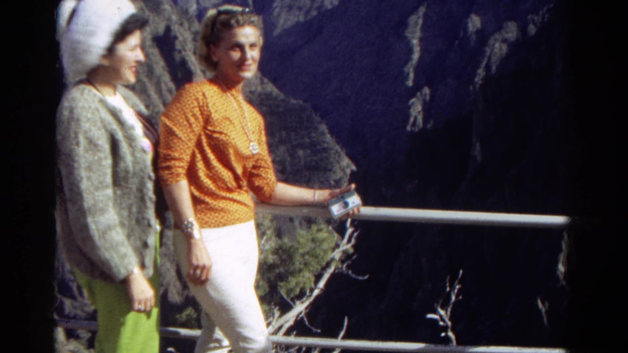 Two women stand side by side at an overlook, one holding a small camera.