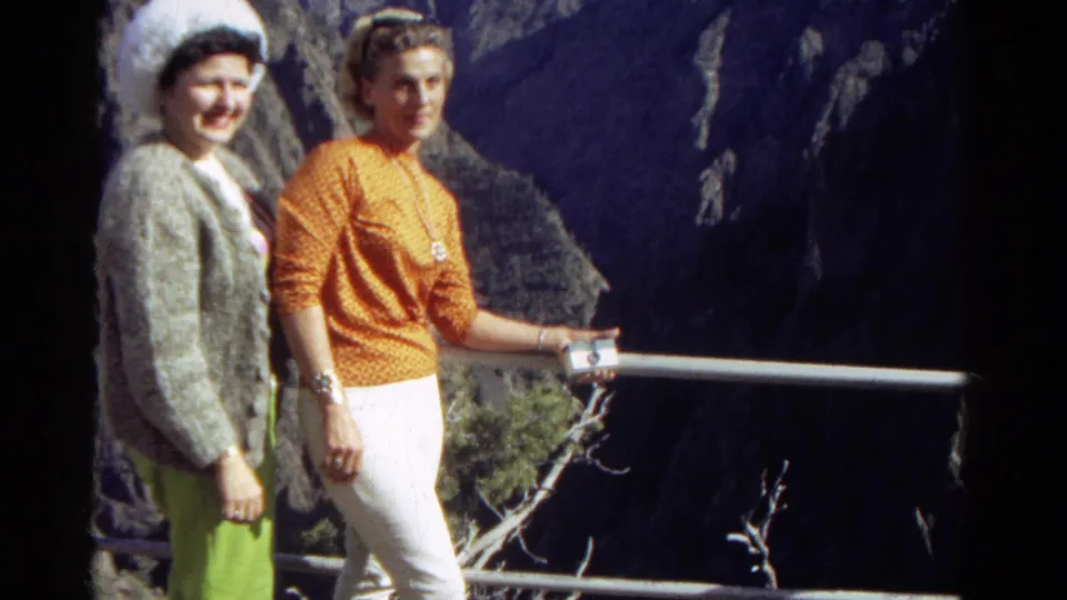 The brief 8mm shot ends with two women still posed at a Colorado scenic overlook, one standing close to the railing.