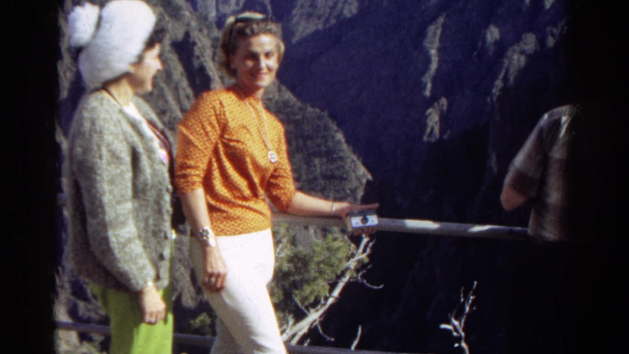 Two women stand at an overlook railing while a partial figure appears at the right edge.