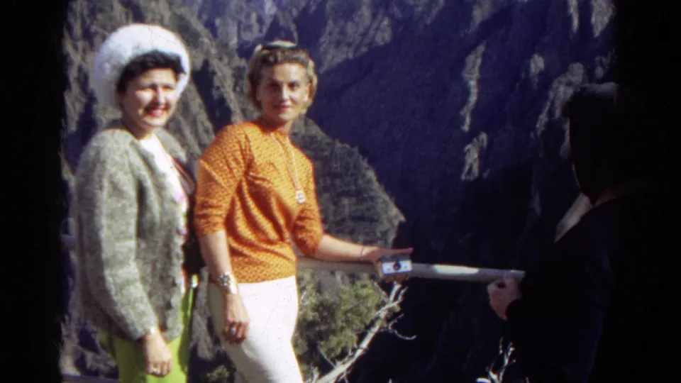 Two women smile toward the camera at a Colorado scenic overlook, with a shadowed person partly visible near the right border.