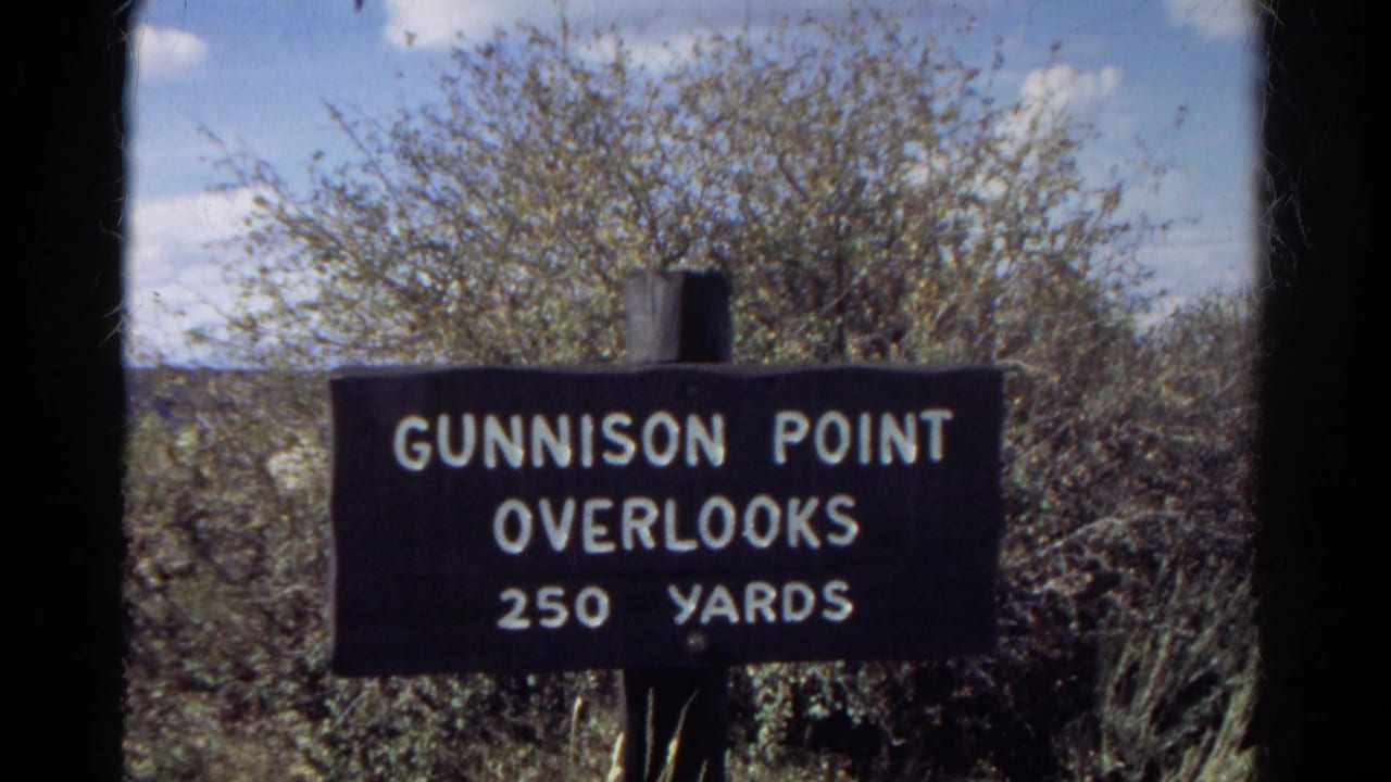 1967 Colorado 8mm frame showing a Gunnison Point Overlooks sign in dry brush under blue sky.