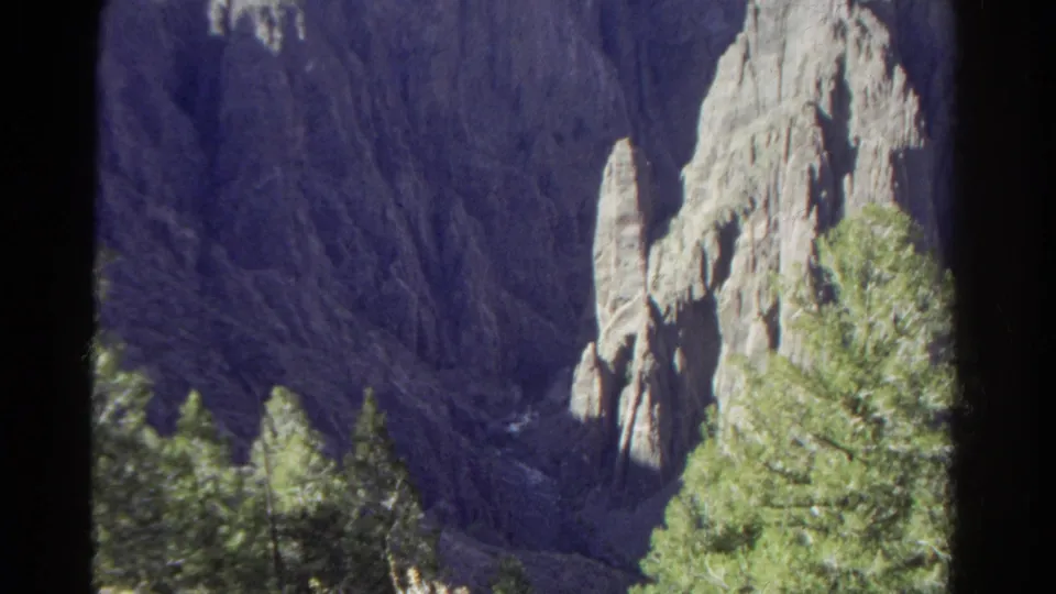 Handheld 8mm frame of a Colorado canyon vista, with vertical rock formations and foreground evergreens.