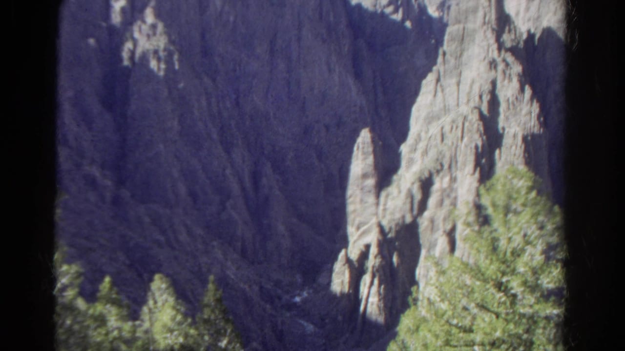 1967 Colorado 8mm frame showing a steep rocky drop, pale cliff faces, and evergreen trees from a high vantage point.