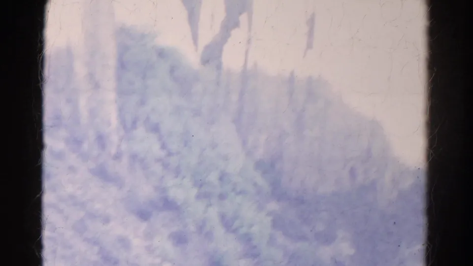 Overexposed 1967 Colorado 8mm frame showing a pale rocky slope, trees, and scrub vegetation near the cliff area.