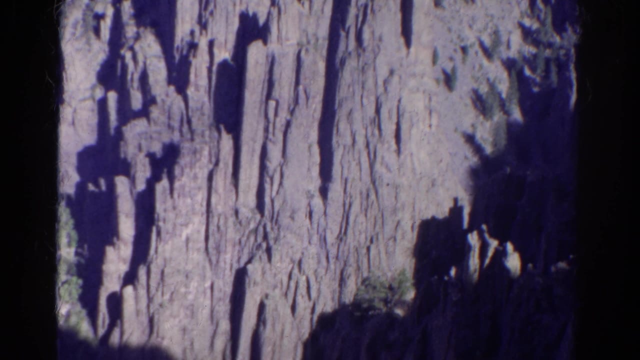 1967 Colorado 8mm frame showing a steep canyon wall with dark shadows, pale vertical rock faces, and small patches of vegetation.