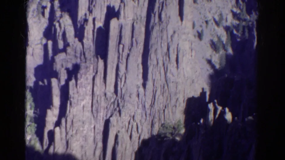 1967 Colorado 8mm frame showing a steep canyon wall with dark shadows, pale vertical rock faces, and small patches of vegetation.