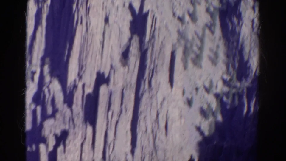 1967 Colorado 8mm frame with a rugged cliff face, dark vertical shadow bands, and blurred vegetation along the upper edge.