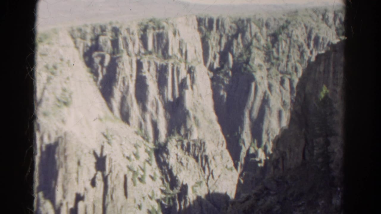 Steep canyon wall with pale rock cliffs and dark film edges.