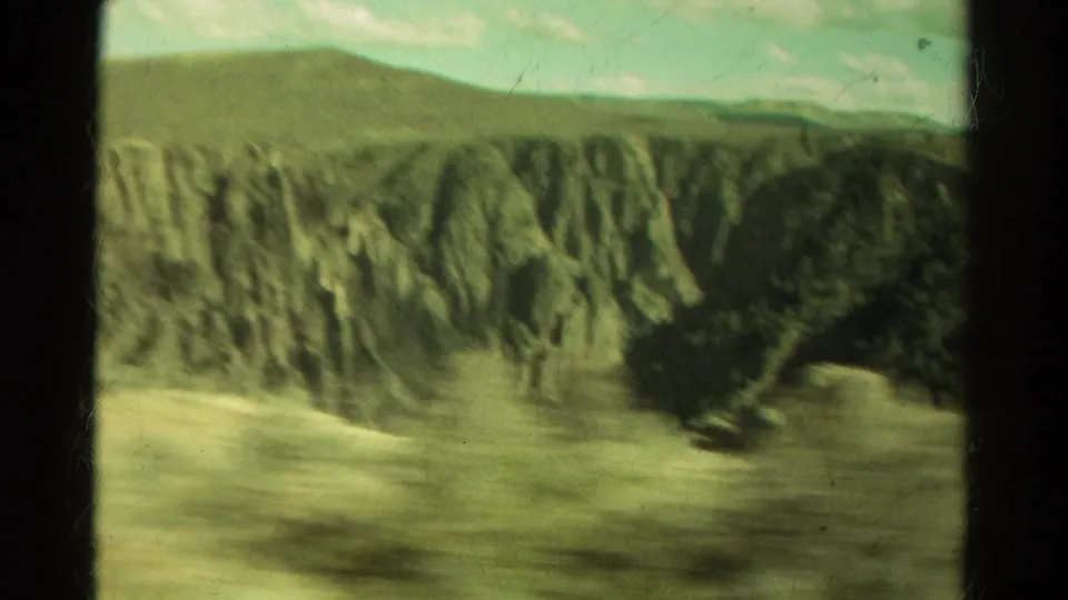Colorado canyon landscape with distant ridges, eroded rock walls, muted green tones, and a brief blue sky visible in 8mm footage.