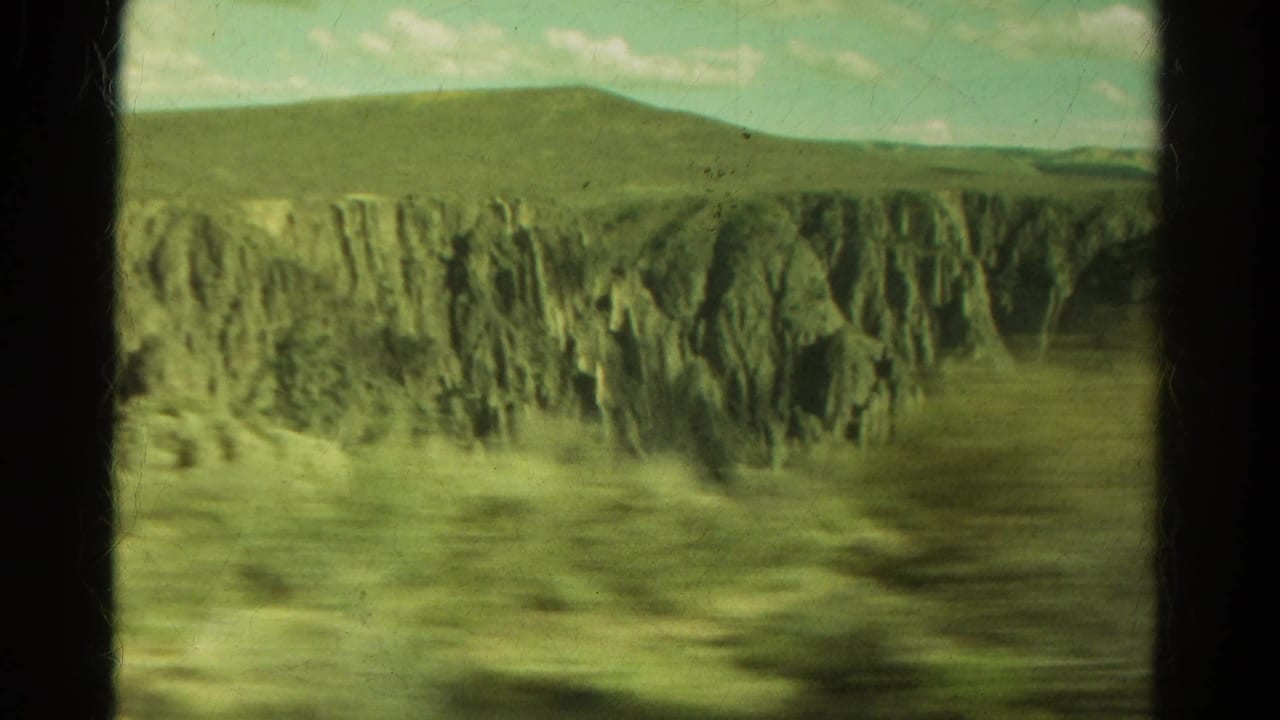 1967 Colorado 8mm travel view from a moving vehicle window, showing steep cliffs, roadside blur, distant hills, and pale sky.