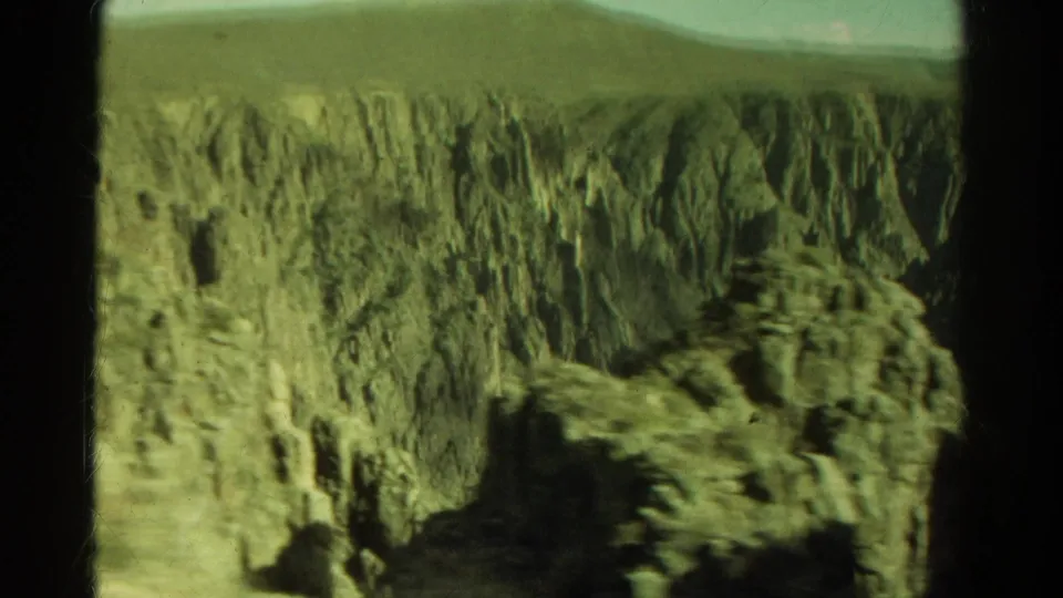1967 Colorado home-movie frame with a steep rocky canyon wall passing outside a vehicle window.