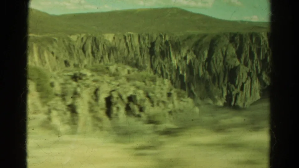 1967 Colorado 8mm frame showing layered canyon cliffs and foreground rock blurred by vehicle movement.