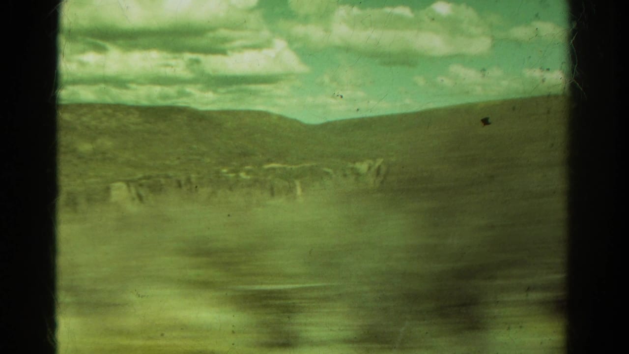 1967 Colorado 8mm frame showing rolling hills, a distant rocky band, cloudy sky, and dark film-frame borders from a moving viewpoint.
