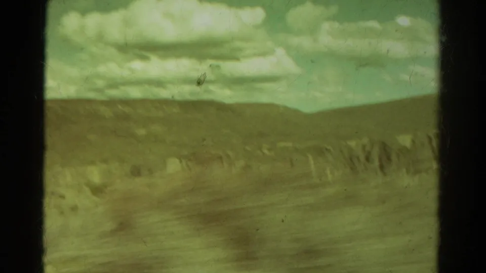 1967 Colorado home-movie still with soft, green-tinted hills, a distant rock line, clouds, and visible film wear.