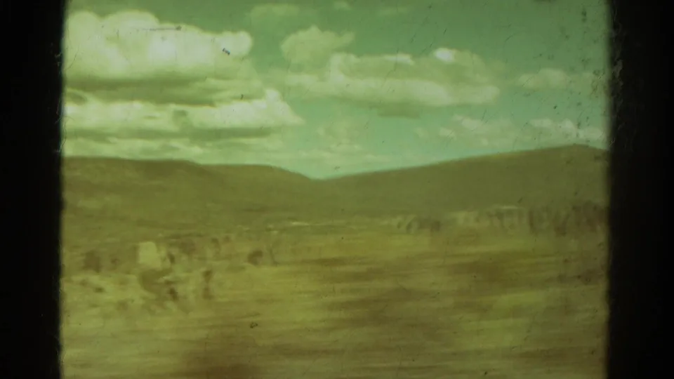 Green-shifted 1967 Colorado 8mm view of low mountains, pale clouds, scrubland, and a distant eroded rock band.