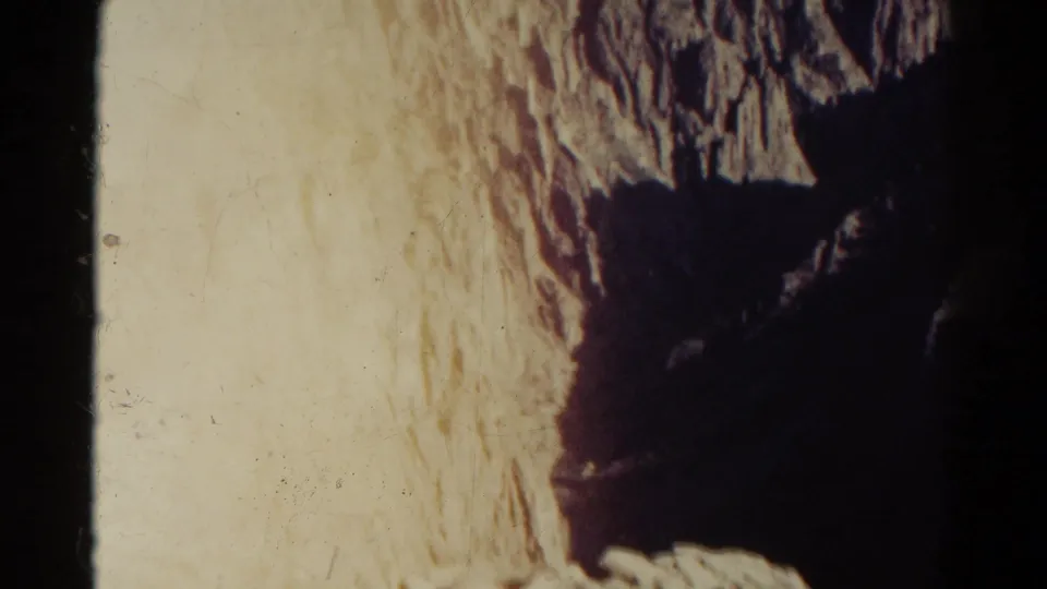 Close 8mm frame of a textured Colorado rock wall, with rough strata, warm exposure, and dark shadow at the edge.