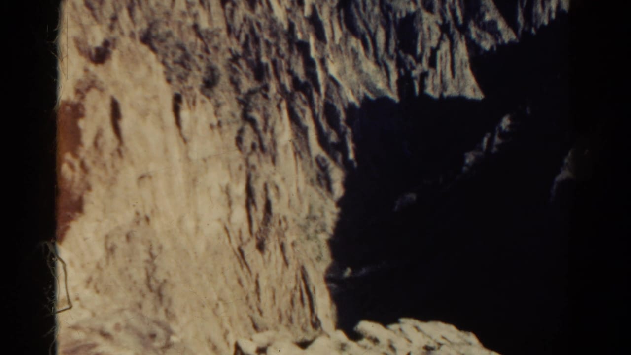1967 Colorado 8mm frame looking down along a rough sunlit rock wall into a deep, shadowed mountain ravine.