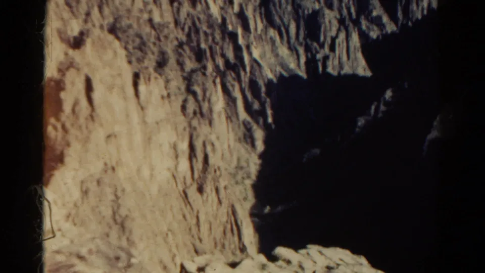1967 Colorado 8mm frame looking down along a rough sunlit rock wall into a deep, shadowed mountain ravine.