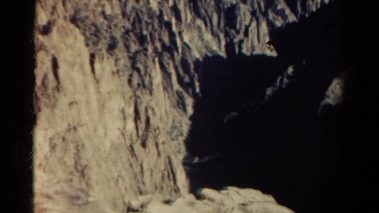 1967 Colorado home-movie frame showing a rugged cliff face beside a dark, steep ravine in late-day light.