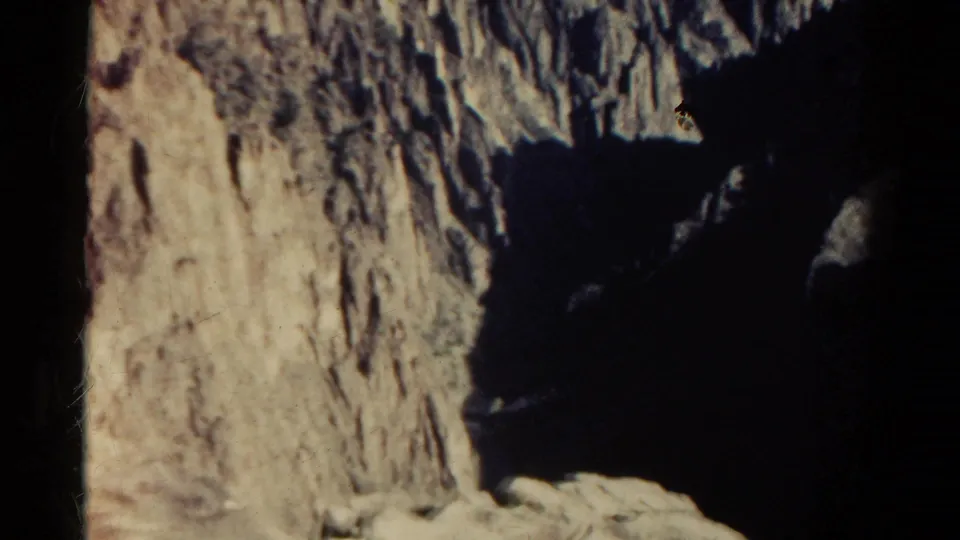 1967 Colorado home-movie frame showing a rugged cliff face beside a dark, steep ravine in late-day light.