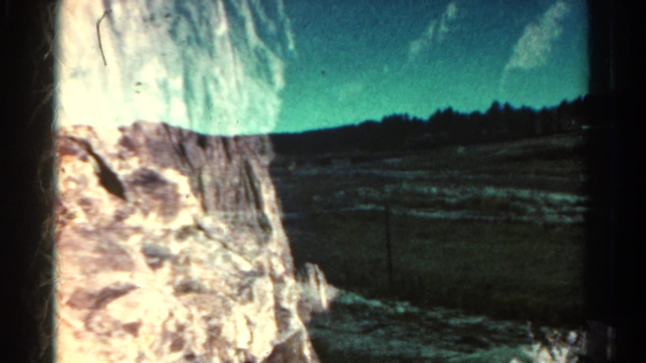 1967 Colorado home-movie frame showing open terrain and distant trees partly obscured by a pale foreground object.