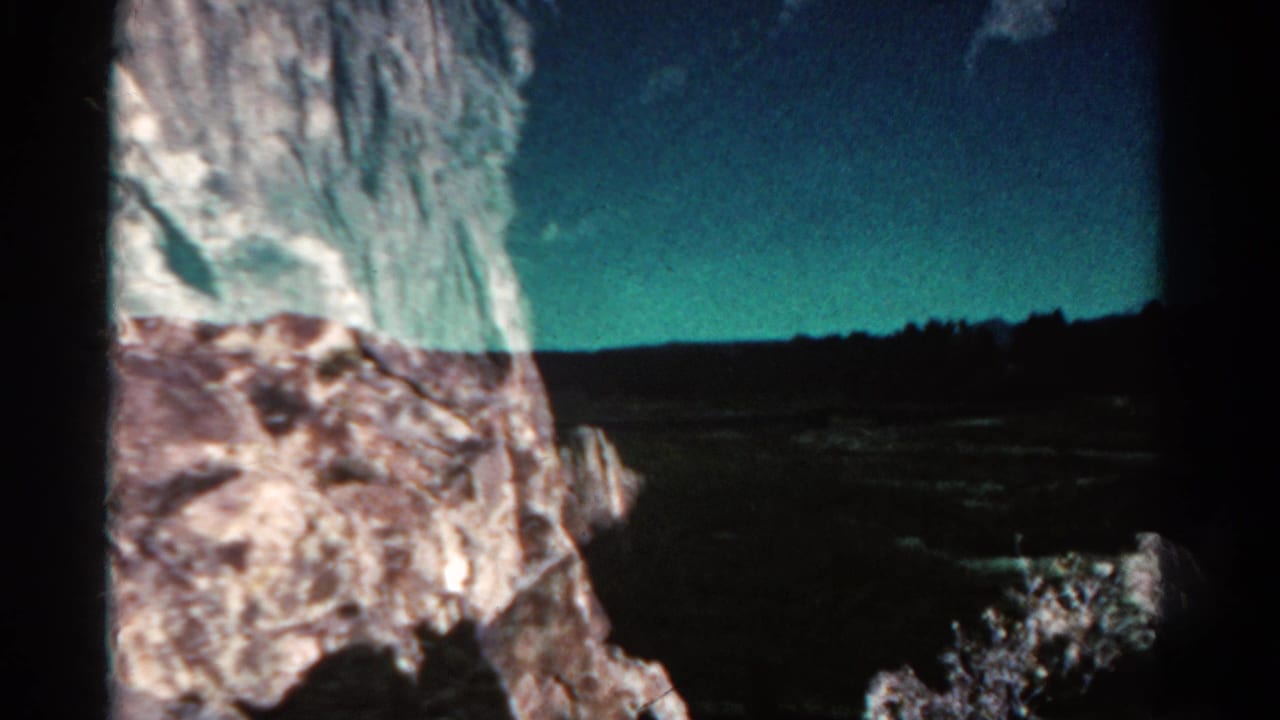 Rock formation at left with open plain, distant horizon, and blue-green sky.
