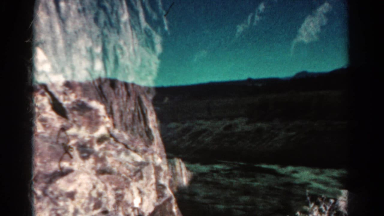 Rock face beside a dark open landscape with low mountains on the horizon.