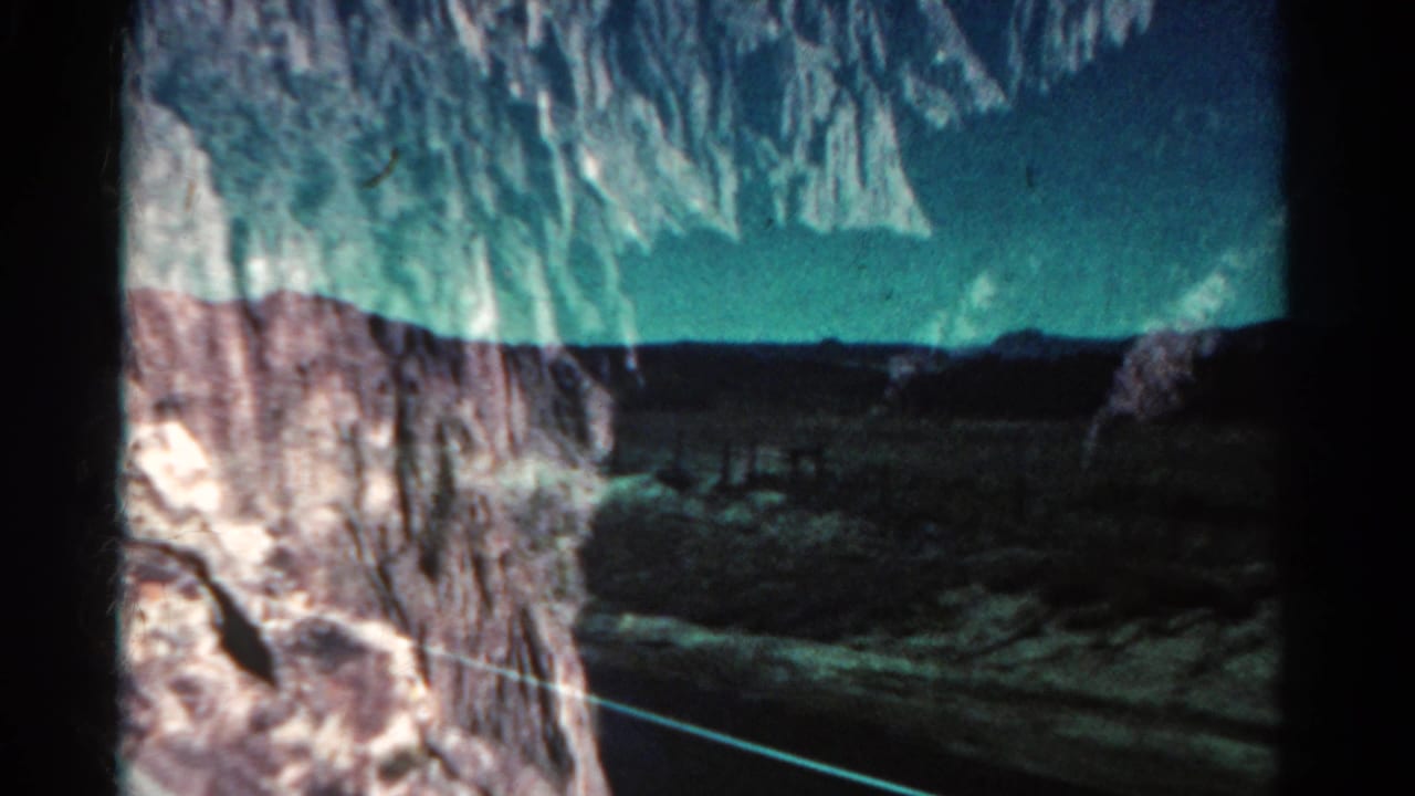 1967 Colorado 8mm frame showing cliffs, distant hills, road edge, and window reflections from a moving car.