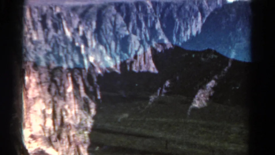 1967 Colorado road-trip frame showing shadowed cliffs, valley floor, distant rock faces, and reflected shapes in the glass.