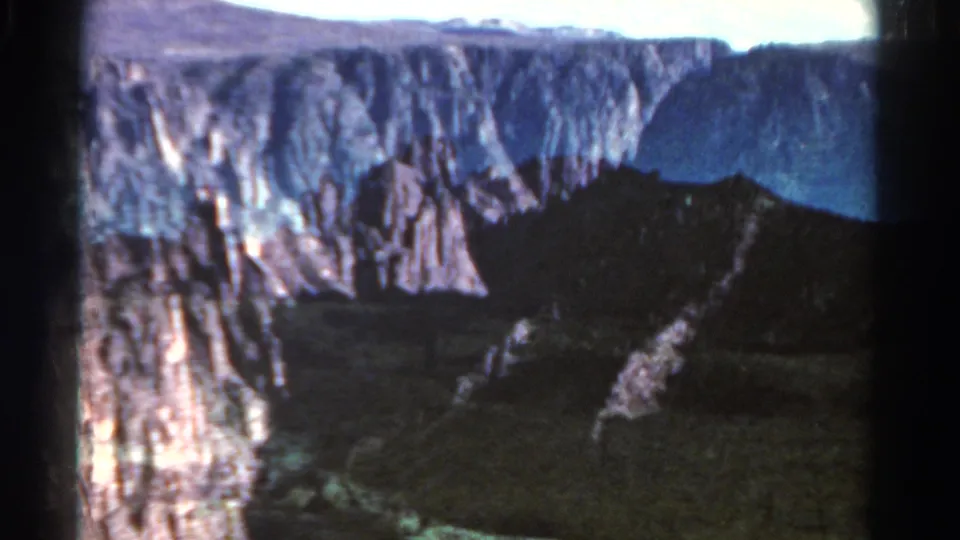1967 Colorado 8mm frame with layered cliffs, a shadowed canyon floor, and soft window reflections from a passing car.