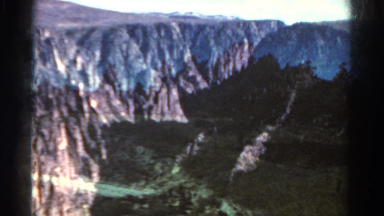 1967 Colorado home-movie frame showing rugged canyon walls, dark trees, and a deep mountain valley.