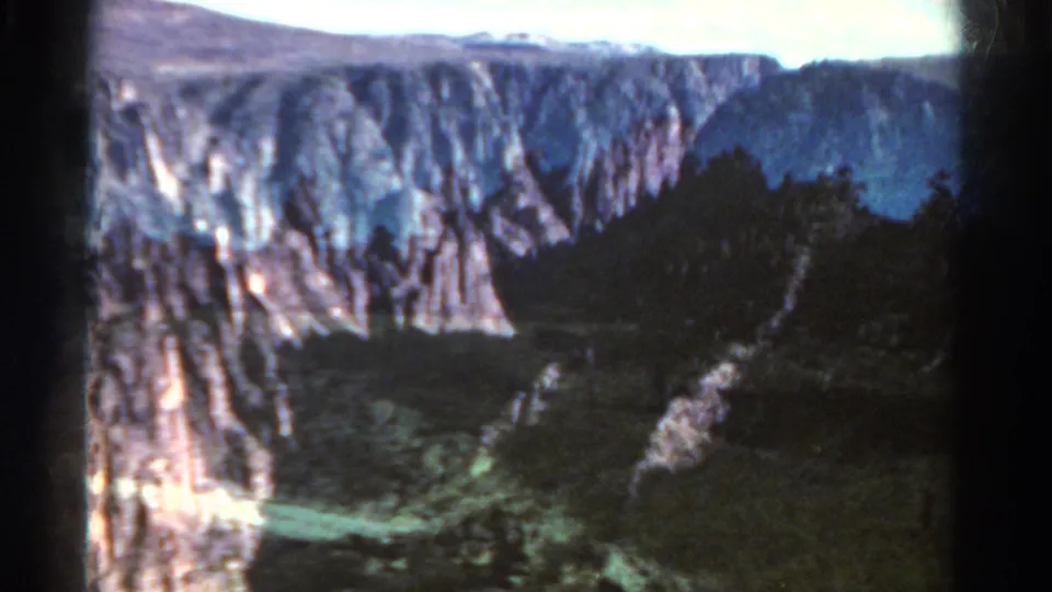 1967 Colorado home-movie frame showing rugged canyon walls, dark trees, and a deep mountain valley.