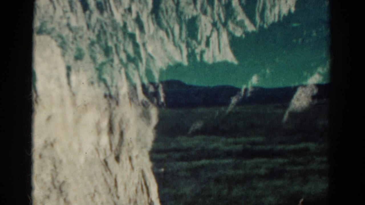 1967 Colorado 8mm frame showing a pale cliff edge, dark valley terrain, distant ridge, and soft blue-green film color.